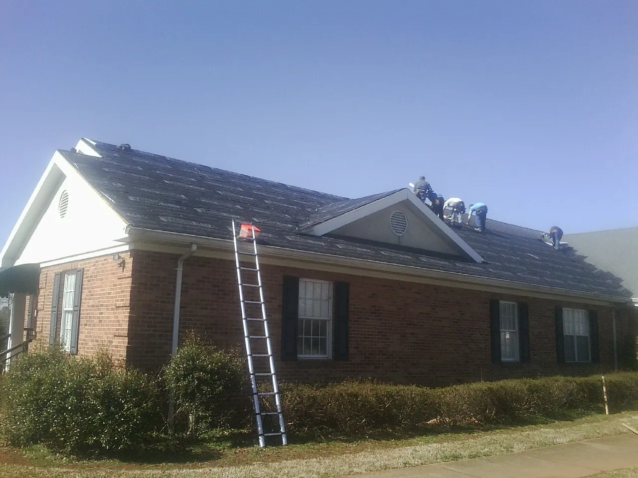 Crew tearing shingles off a brick ranch roof with a ladder set — Emergency Roof Repair work by our crew in Forestdale